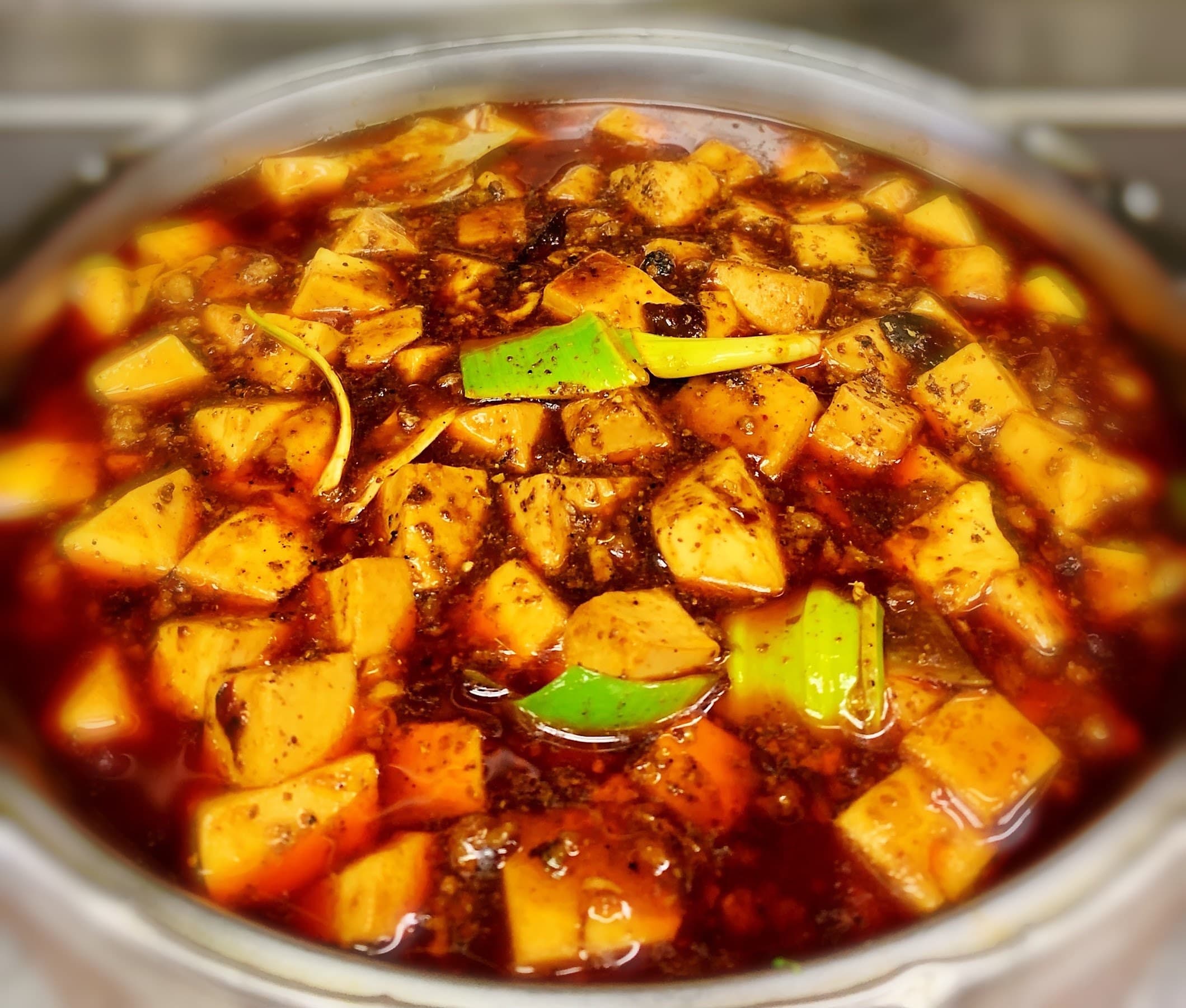 A bowl of mapo tofu in crimson chili oil with scallions